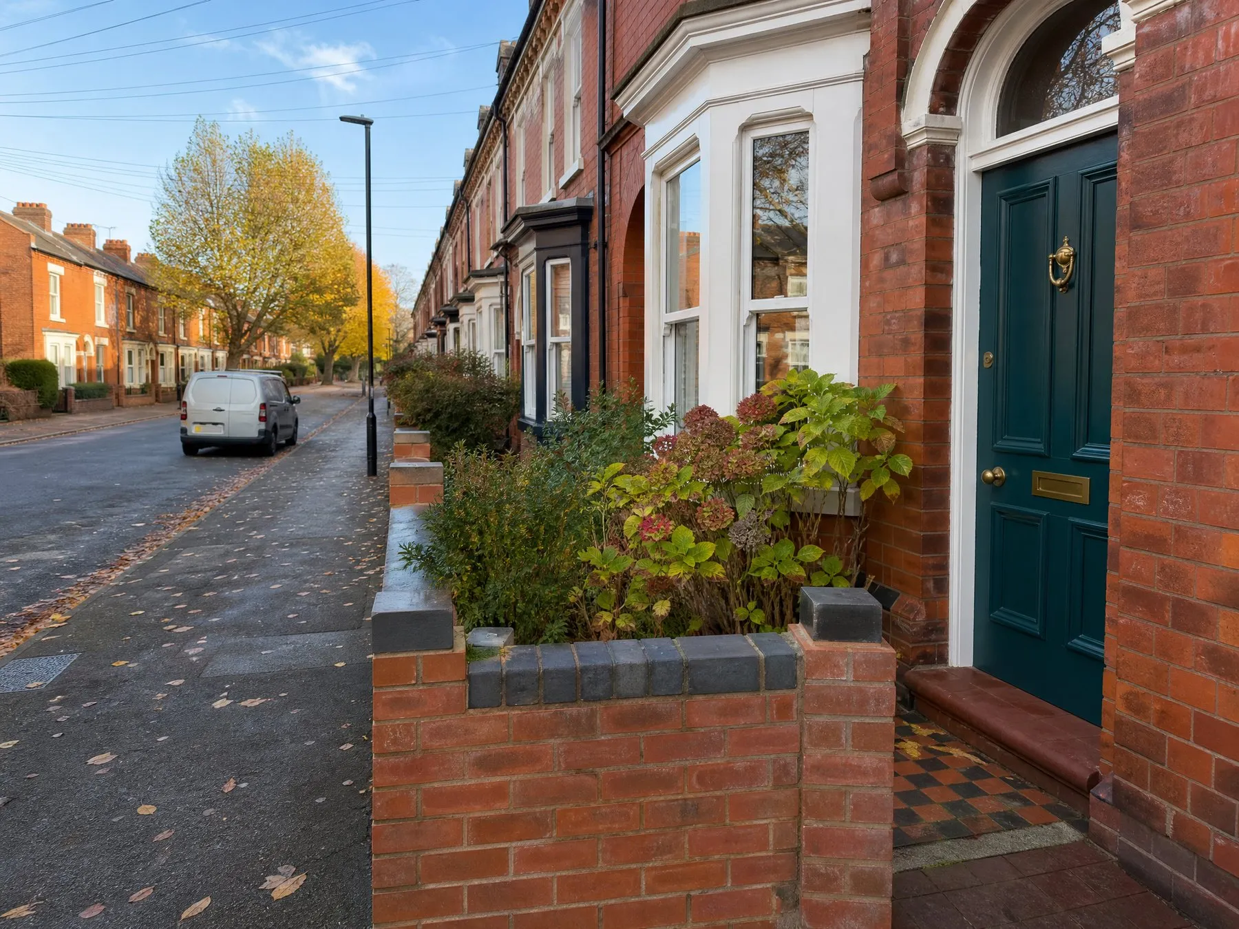 A red-brick terraced street in autumn with a teal front door in the foreground